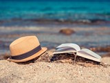 Sonnenhut und Buch am Strand vor dem blauen Meer