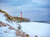 Schneebedeckte Dünen an der rauhen Norsee mit Leuchturm