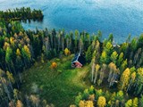 Luftaufnahme eines roten Blockhauses mit Sauna im Frühlingswald am See in Finnland 