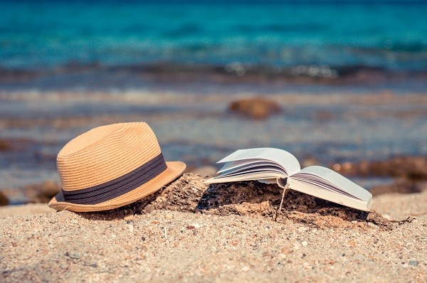 Sonnenhut und Buch am Strand vor dem blauen Meer