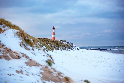 Schneebedeckte Dünen an der rauhen Norsee mit Leuchturm