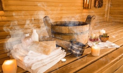 Dampfender Kübel in der Sauna mit Kerzenschein und Handtüchern