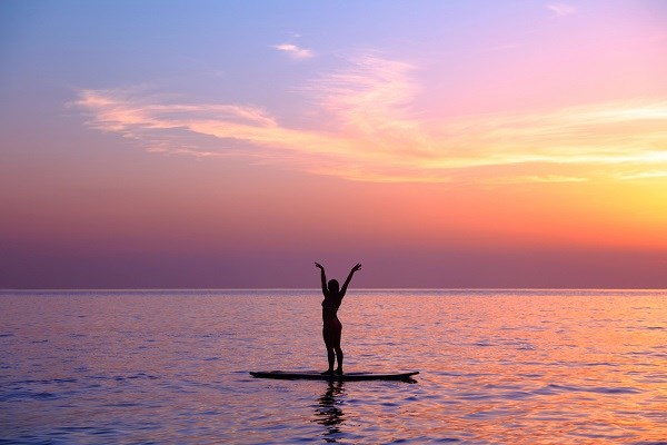 Eine Frau macht Yoga auf einem SUP-Board im Sonnenuntergang.