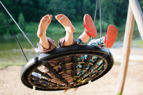 Kinder schaukeln auf einer großen Korbschaukel auf einem Spielplatz im Park 