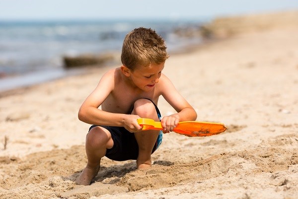 Kleiner Junge mit Plastikschaufel am Strand in Dänemark