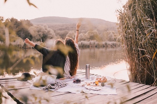 Zwei Freundinnen machen ein Picknick im Herbstwald in der Nähe eines Sees