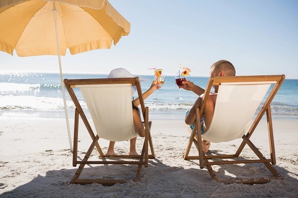 Ein Paar sitzt am Strand in Sonnenstühlen und stößt mit Drinks an